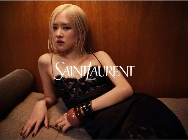 Blonde woman wearing a black slip dress with lace trim reclining on a brown sofa, photographed by Gray Sorrenti.