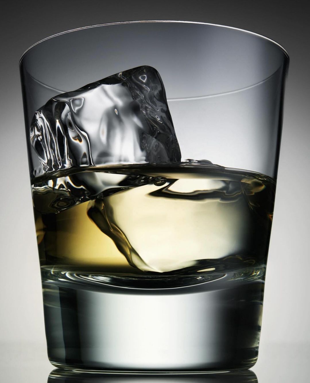 Glass of amber liquor with a single ice cube, beverage photography showcasing a clear drink with ice in a lowball glass.