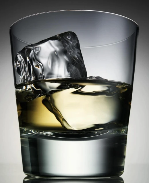 Glass of amber liquor with a single ice cube, beverage photography showcasing a clear drink with ice in a lowball glass.