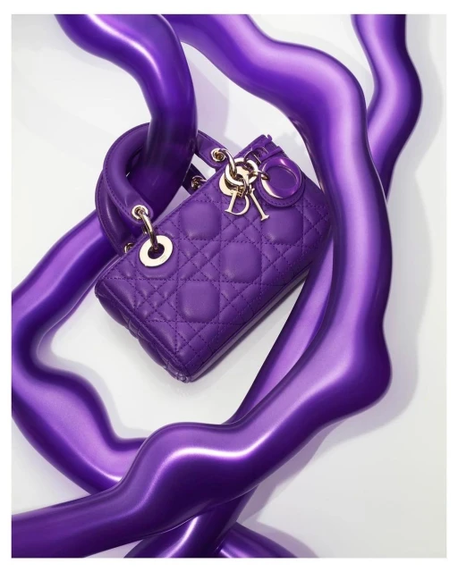 Elegant, quilted Lady Dior handbag in vibrant purple with gold hardware, gracefully intertwined with glossy, abstract purple forms.