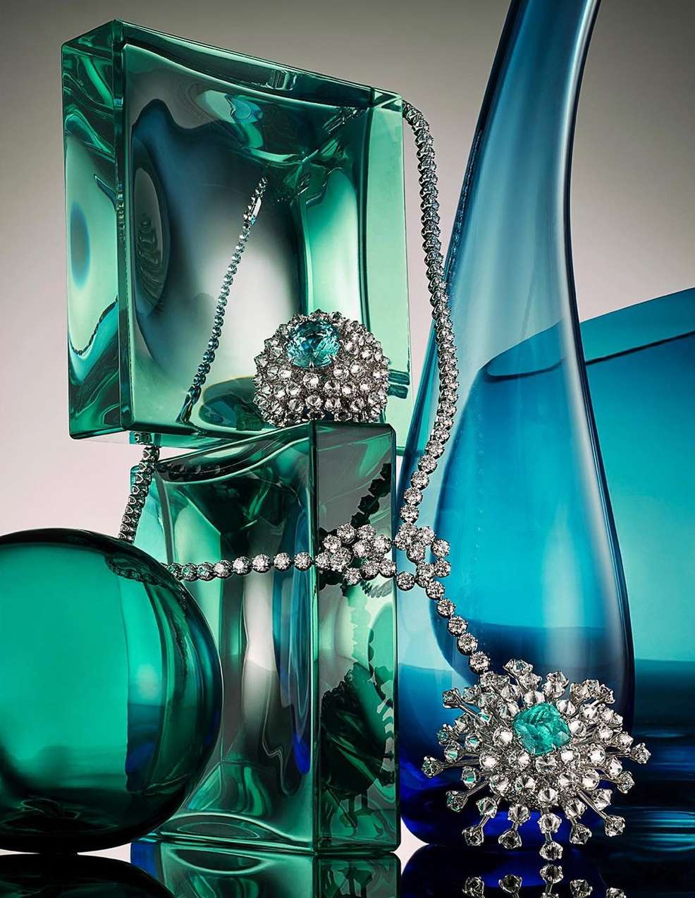 Elegant jewelry still life: diamond necklace and gemstone ring displayed on decorative translucent aqua blue and green glass blocks.