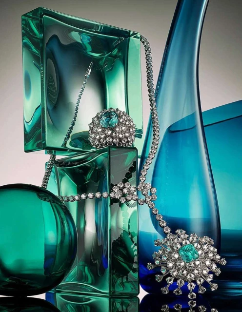Elegant jewelry still life: diamond necklace and gemstone ring displayed on decorative translucent aqua blue and green glass blocks.