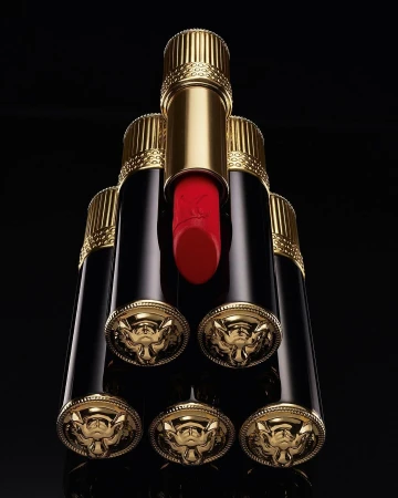 Luxury beauty still life: A pyramid arrangement of gold and black lipsticks with red visible on the top one against a black background.
