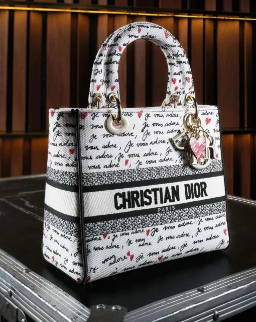Christian Dior handbag featuring a white canvas exterior printed with black handwriting and red hearts, complemented by gold hardware.