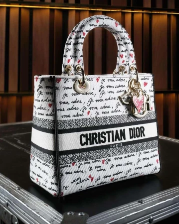 Christian Dior handbag featuring a white canvas exterior printed with black handwriting and red hearts, complemented by gold hardware.