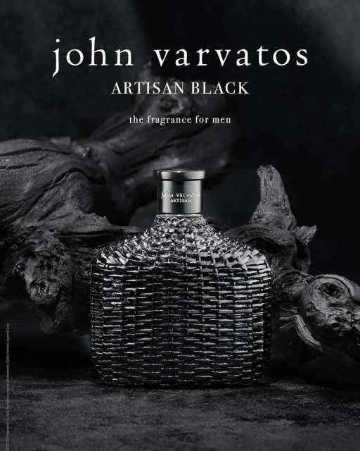 John Varvatos Artisan Black fragrance bottle close-up, displayed on a dark wooden surface against a blurred black background.
