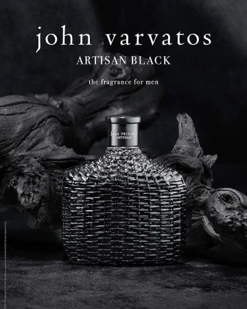 John Varvatos Artisan Black fragrance bottle close-up, displayed on a dark wooden surface against a blurred black background.