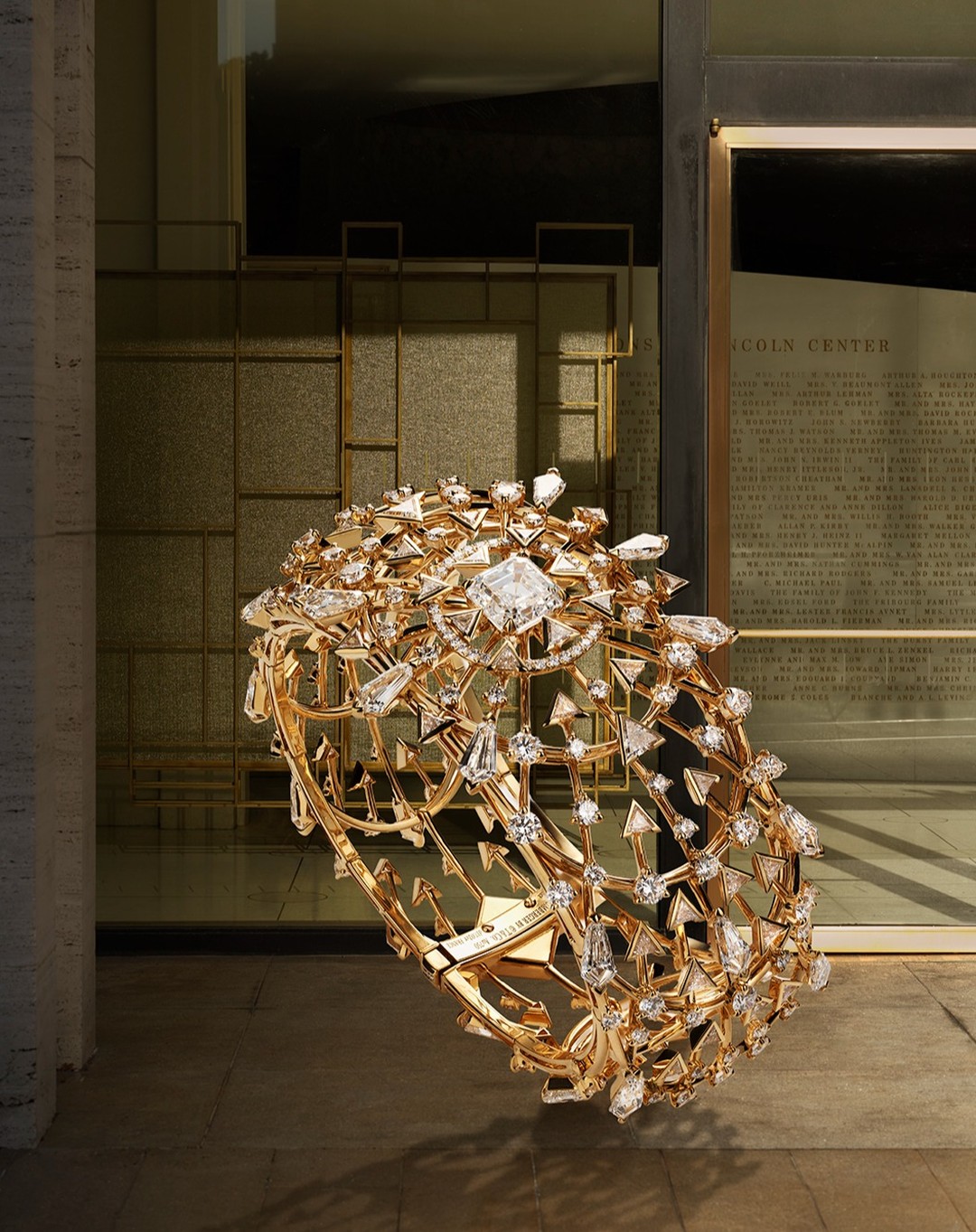 Luxury gold cuff bracelet adorned with diamonds and crystals set against a neutral background with architectural elements in the backdrop.