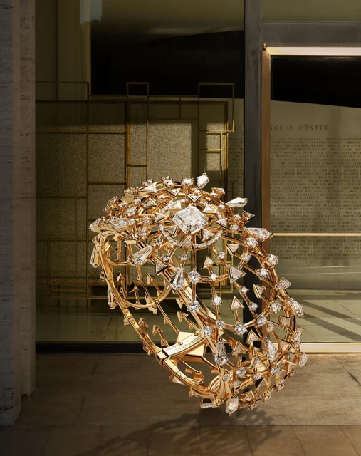 Luxury gold cuff bracelet adorned with diamonds and crystals set against a neutral background with architectural elements in the backdrop.