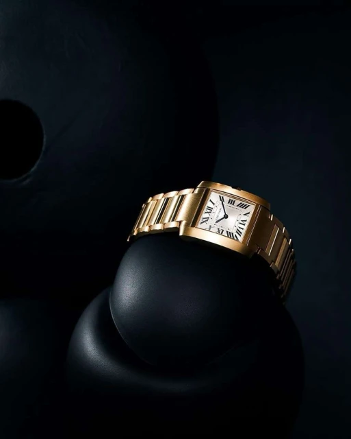 Elegant gold wristwatch with a white face displayed against black abstract forms creating a minimalist and luxurious product shot.