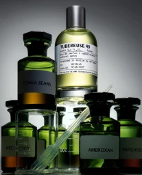 Arrangement of green glass perfume bottles and apothecary jars with white labels against a grey gradient background