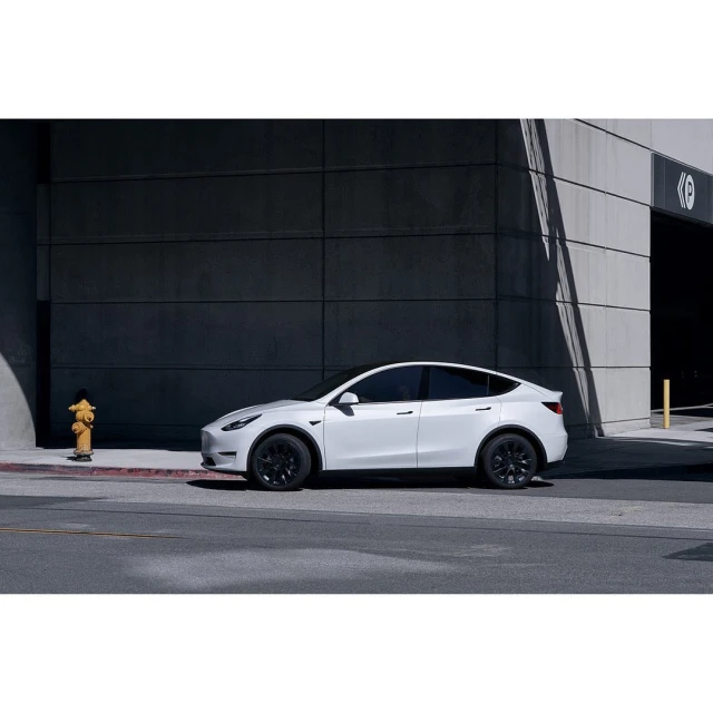 White Tesla Model Y parked on a city street with modern building and fire hydrant in the background, offering a sleek and urban aesthetic.