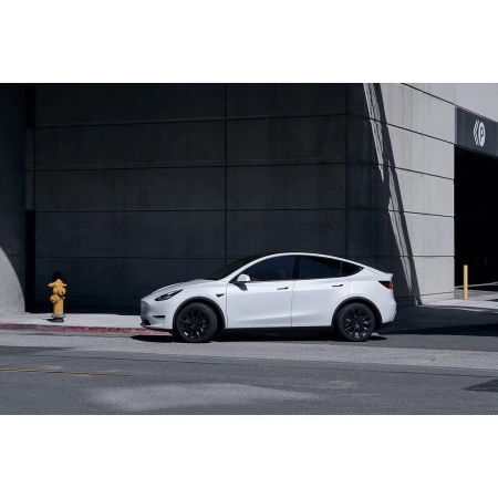 White Tesla Model Y parked on a city street with modern building and fire hydrant in the background, offering a sleek and urban aesthetic.