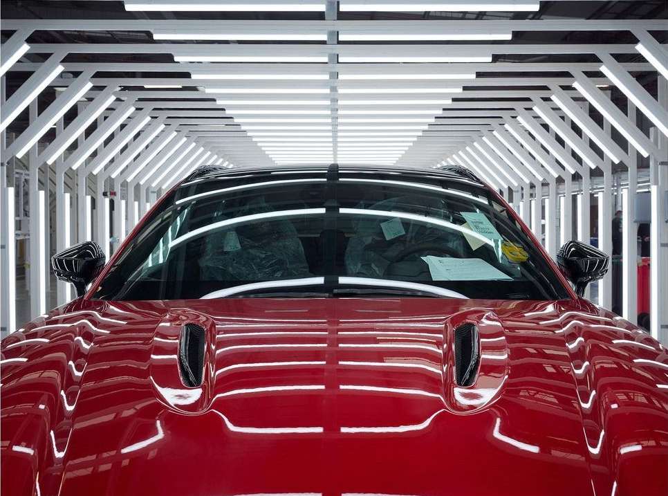 Front view of a red sports car under bright studio lights, showcasing automotive design and manufacturing process with a modern aesthetic.