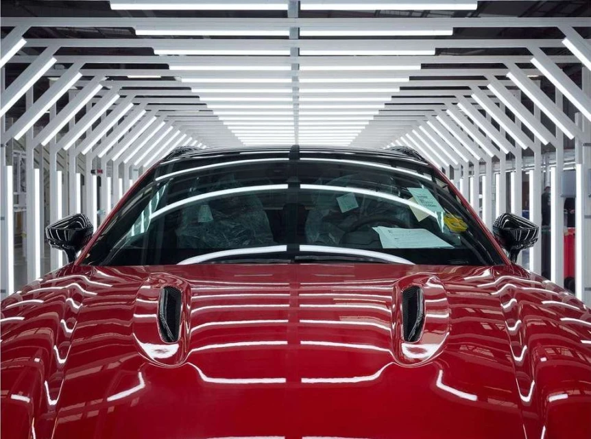 Front view of a red sports car under bright studio lights, showcasing automotive design and manufacturing process with a modern aesthetic.