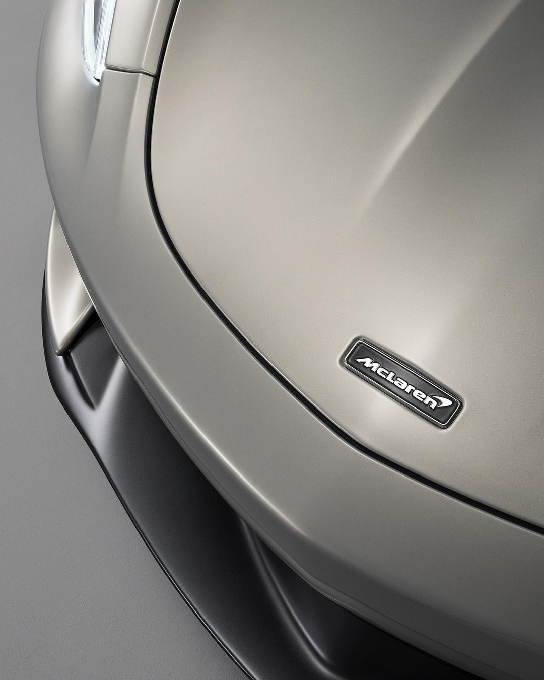 Close-up of a silver McLaren car hood with the company logo. Focus on the car's sleek lines and reflective surface.