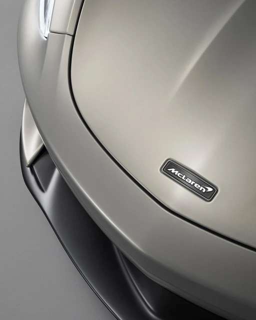 Close-up of a silver McLaren car hood with the company logo. Focus on the car's sleek lines and reflective surface.