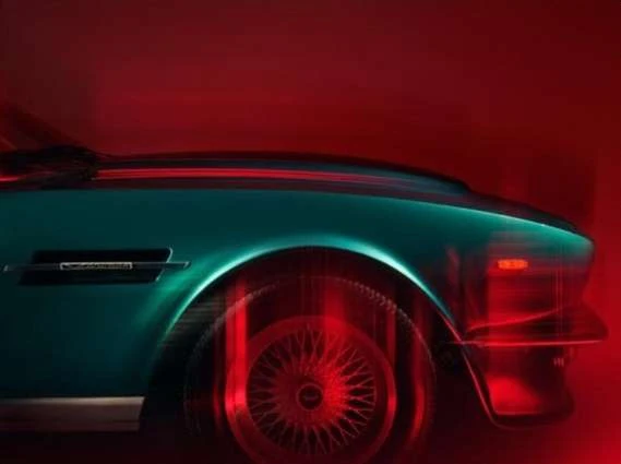 Teal vintage car side profile showing the wheel and front end details with soft red lighting against a red background.