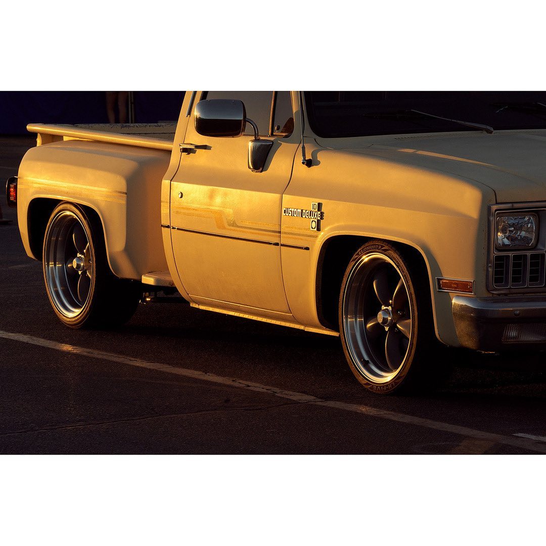 Vintage tan Chevrolet C10 pickup truck in an outdoor setting, featuring custom wheels and lowrider styling in golden light.