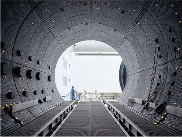 Interior view of a large, dark, tunnel-like industrial space, showing a distant figure in protective wear walking along a pathway.