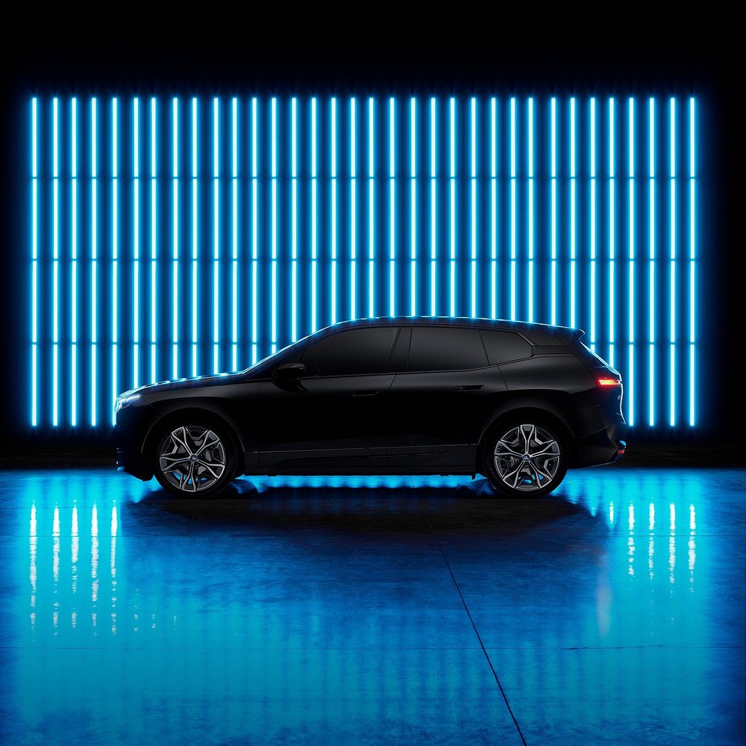 Side view of a dark metallic SUV car parked indoors on a reflective surface with blue neon lights in the dark background.