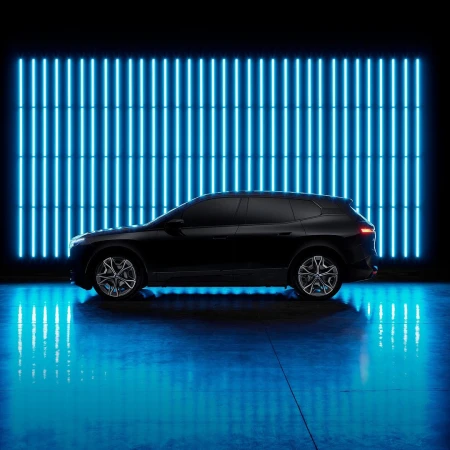 Side view of a dark metallic SUV car parked indoors on a reflective surface with blue neon lights in the dark background.