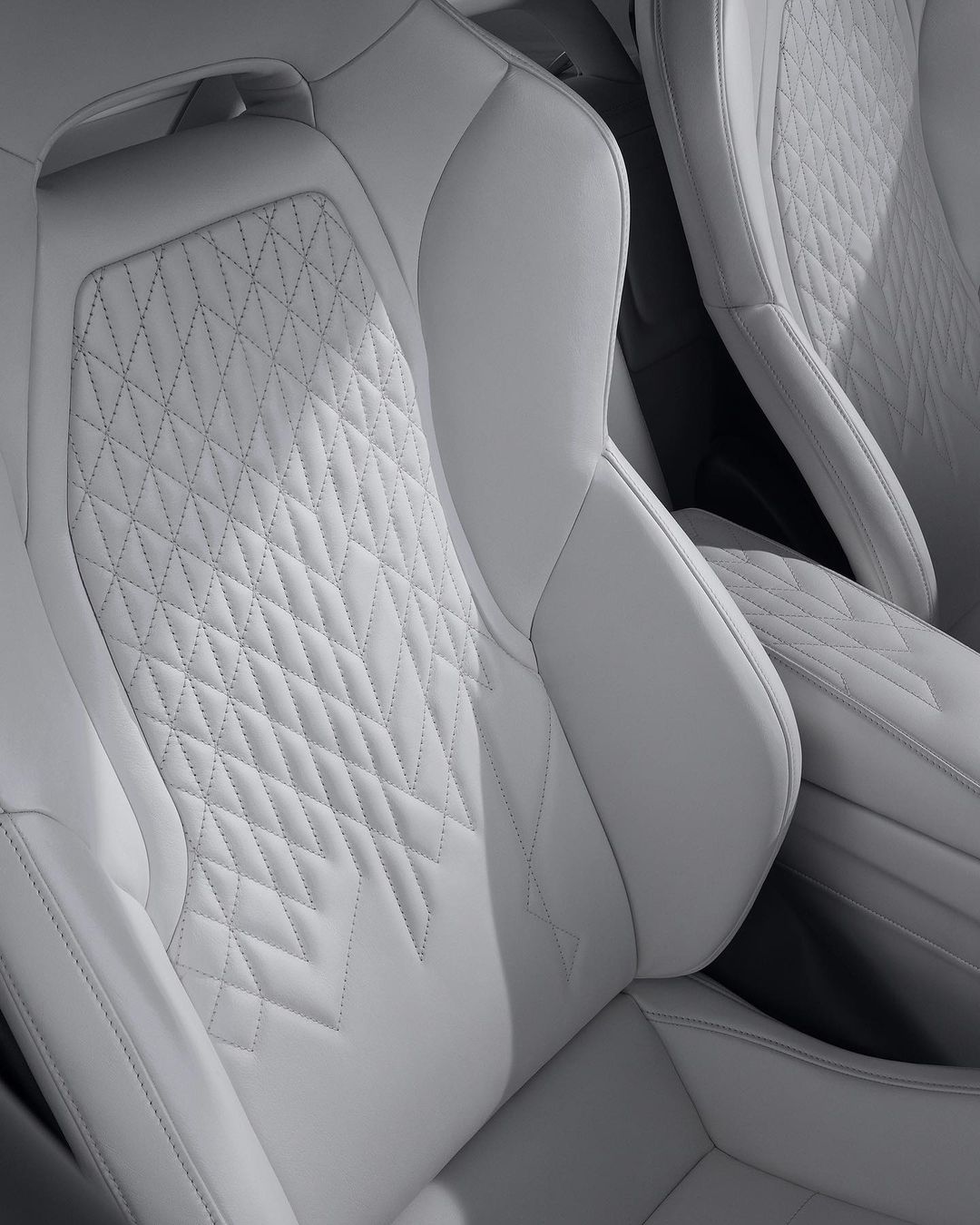 Close-up of white leather car seats featuring diamond stitching and intricate detailing, showcasing automotive interior design.