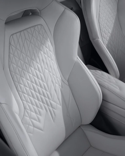 Close-up of white leather car seats featuring diamond stitching and intricate detailing, showcasing automotive interior design.