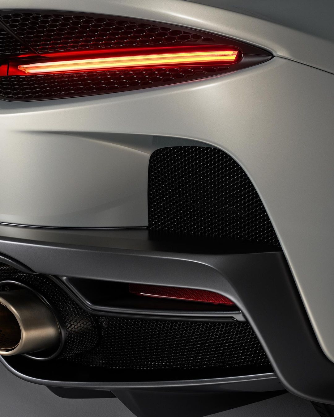 Close-up of the rear of a gray sports car, featuring a modern taillight, black grille, and exhaust pipe.