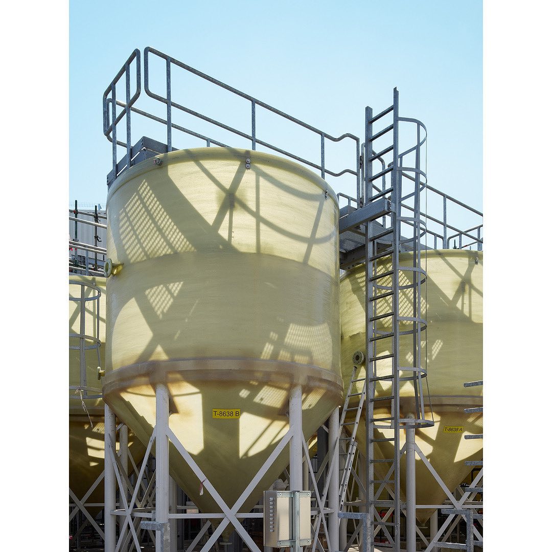 Industrial view of large, tall storage tanks with metal frame support, ladders, and railings under a clear blue sky during daytime.