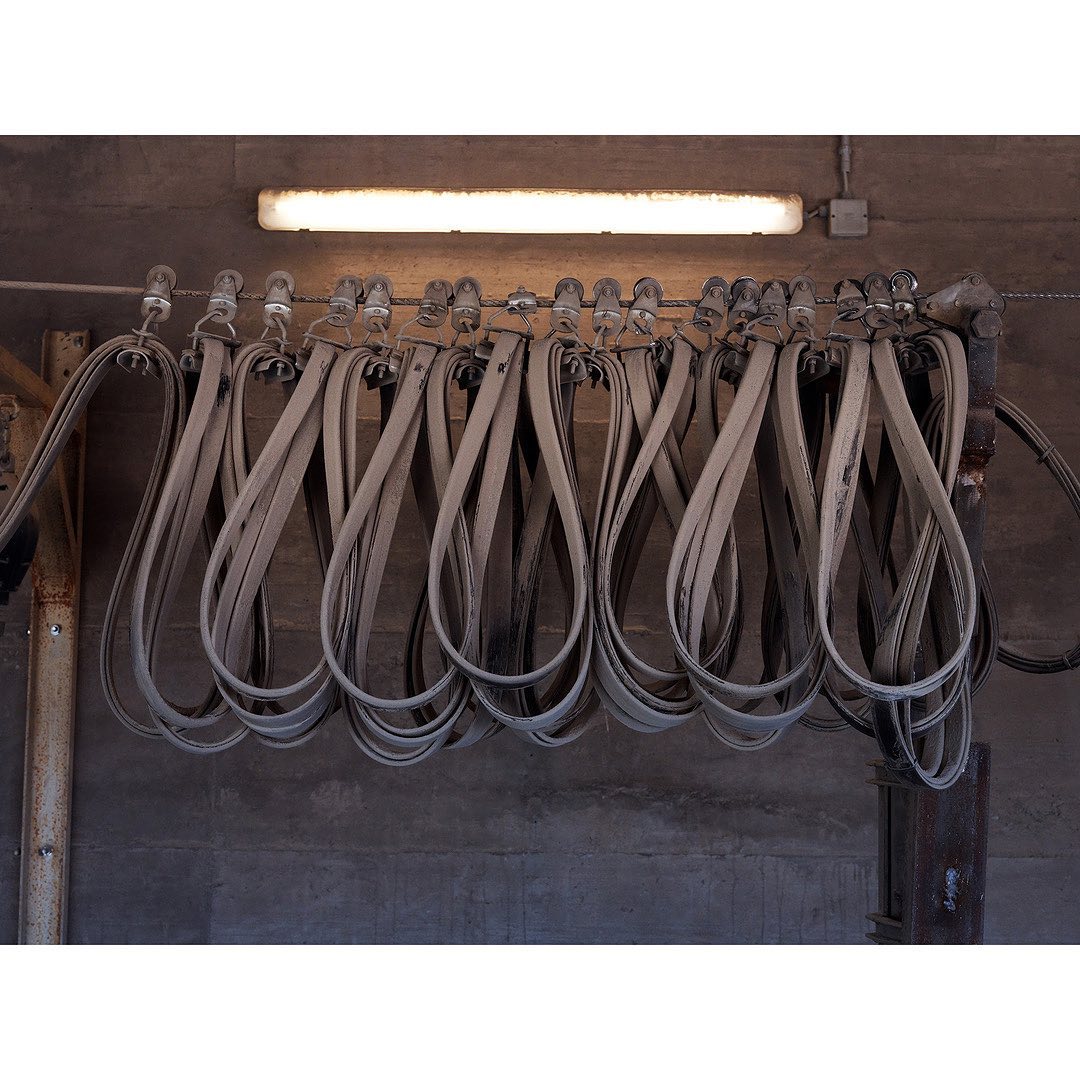 Industrial scene featuring a row of grey industrial belts hanging from metal hooks beneath a fluorescent light fixture, creating a repetitive pattern.