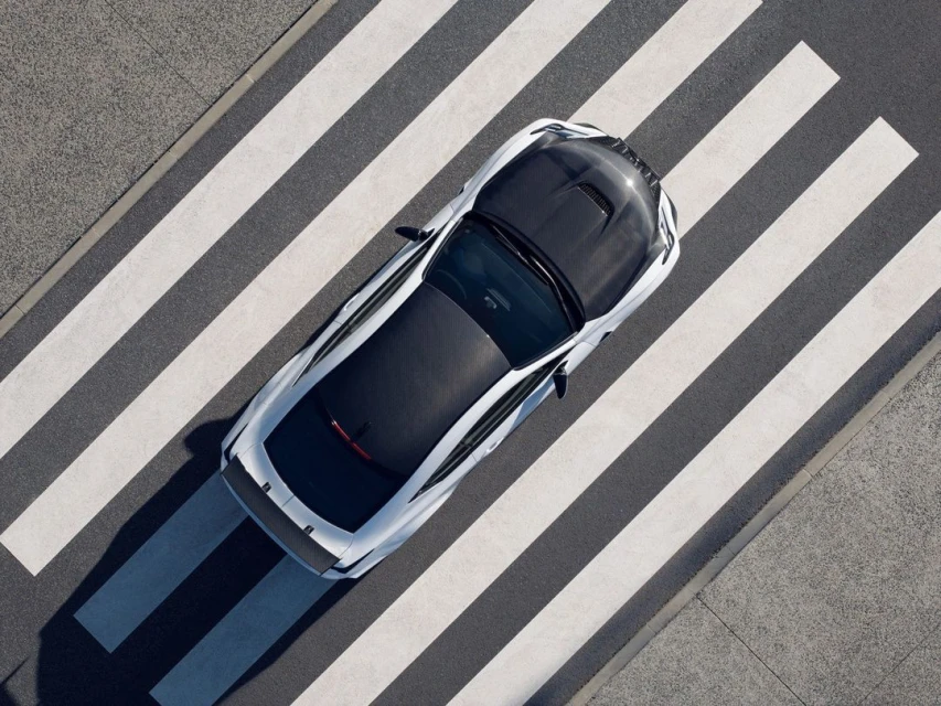 Aerial view of a sleek white and black sports car crossing a pedestrian crosswalk with asphalt. The car is centered and angled.