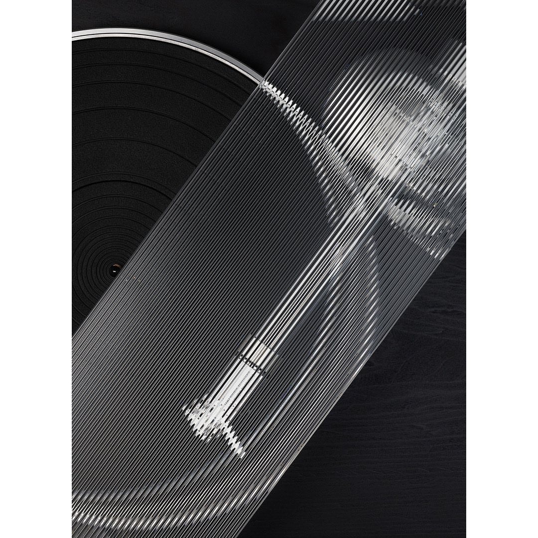 Close-up of a vinyl record player with clear grooved top, emphasizing the texture and patterns in a monochrome palette of blacks and grays.