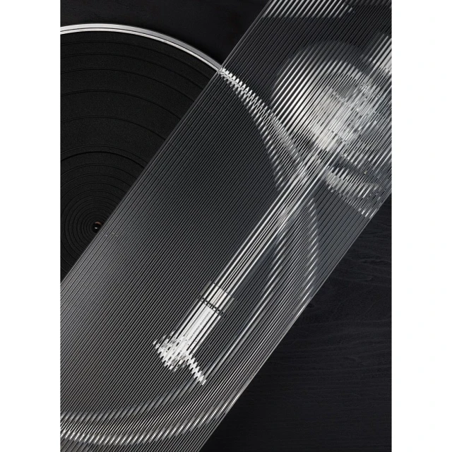 Close-up of a vinyl record player with clear grooved top, emphasizing the texture and patterns in a monochrome palette of blacks and grays.
