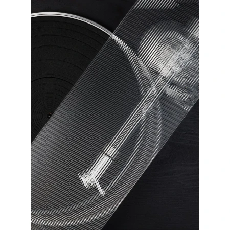 Close-up of a vinyl record player with clear grooved top, emphasizing the texture and patterns in a monochrome palette of blacks and grays.