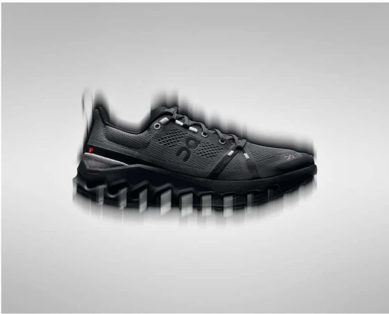 Close-up product shot of a black running shoe with motion blur effects against a gradient grey studio backdrop.