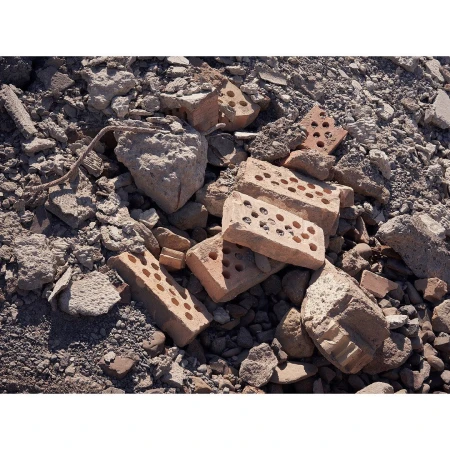 Pile of broken red bricks and grey rocks under bright lighting in a construction or demolition site, showcasing textures and decay.