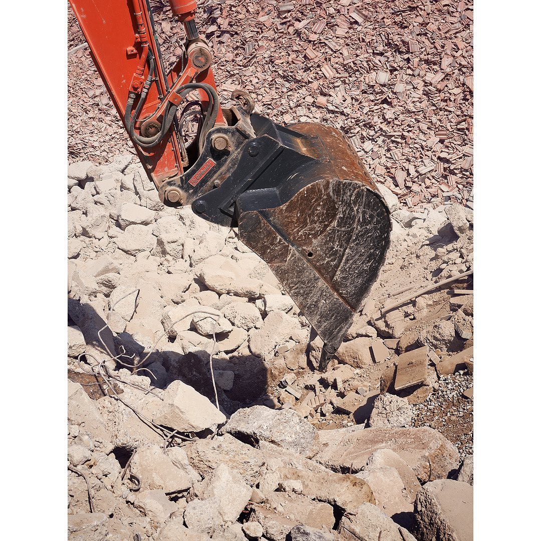 Excavator bucket arm angled towards rubble and dirt, positioned for construction or demolition work in the outdoor environment. 