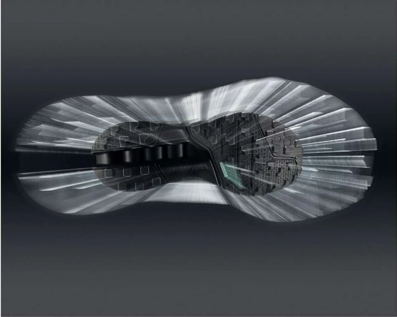 Sole of a black sneaker displayed with a motion effect, showcasing its design and construction against a gradient grey background.