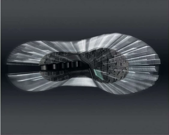 Sole of a black sneaker displayed with a motion effect, showcasing its design and construction against a gradient grey background.
