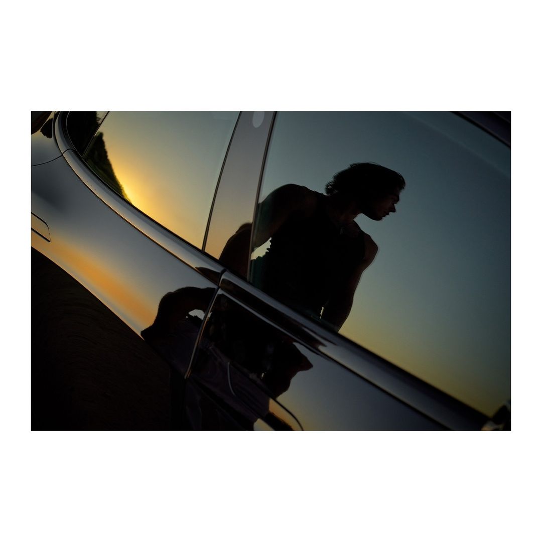 Car reflection showcases an adult male silhouette against a sunset backdrop, highlighting automotive design and evening light.