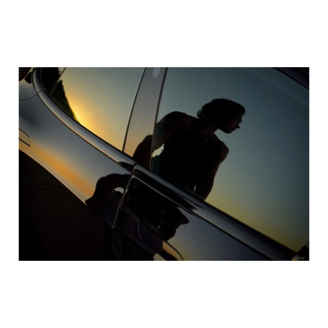 Car reflection showcases an adult male silhouette against a sunset backdrop, highlighting automotive design and evening light.