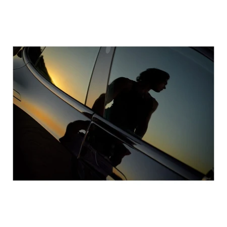 Car reflection showcases an adult male silhouette against a sunset backdrop, highlighting automotive design and evening light.