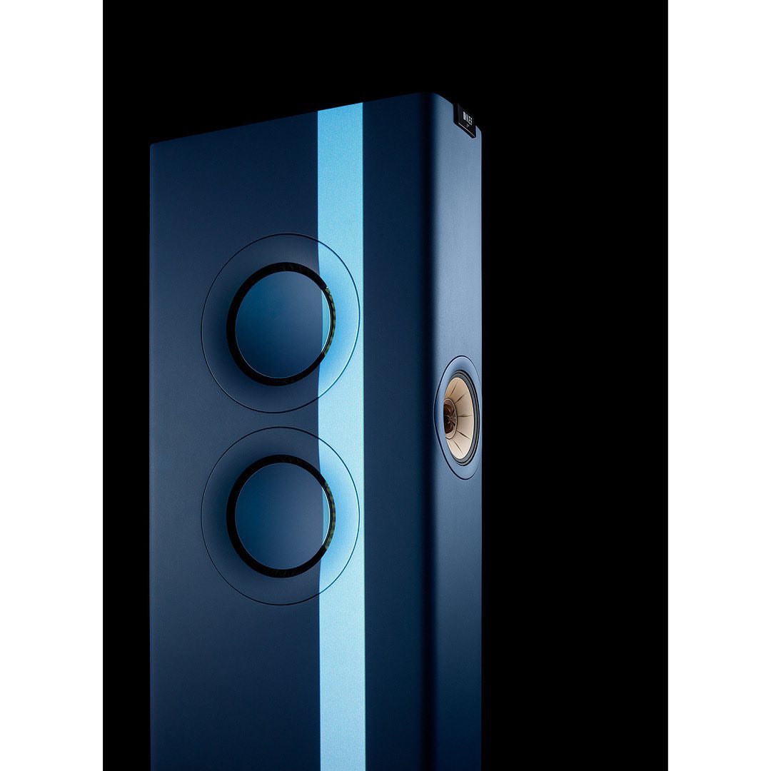 A vertical, front-facing shot of a blue KEF LS60 Wireless speaker with a light blue vertical stripe, displayed against a black background.
