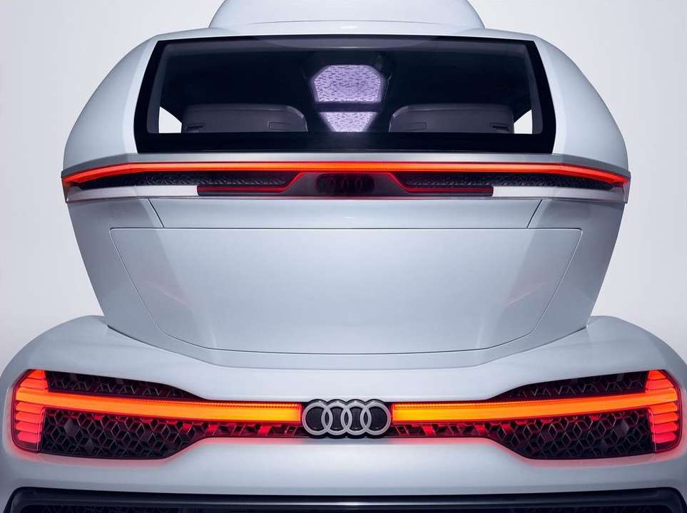 A rear view of a white concept car showcases sleek design, red taillights, and the Audi logo against a clean, neutral background.