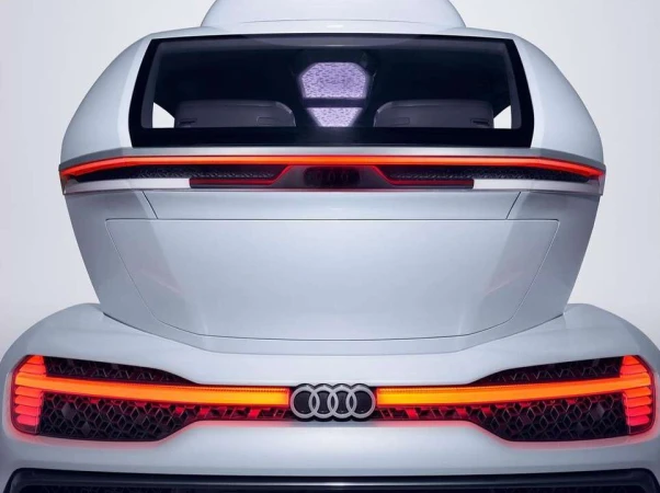 A rear view of a white concept car showcases sleek design, red taillights, and the Audi logo against a clean, neutral background.