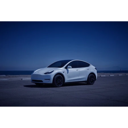 Tesla Model Y parked near the coast under a blue sky, showcasing its sleek design and the vehicle's presence in a scenic outdoor setting.