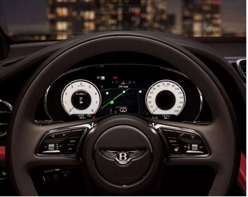 Close-up of a Bentley steering wheel and dashboard, with illuminated gauges and off-road navigation visible in an elegant interior.