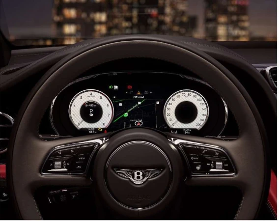 Close-up of a Bentley steering wheel and dashboard, with illuminated gauges and off-road navigation visible in an elegant interior.