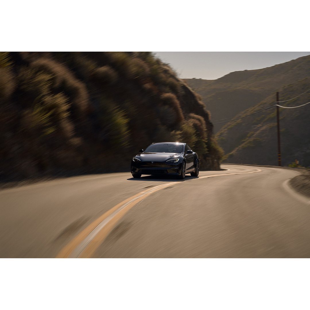 Black electric car drives on a winding road through mountainous landscape on a sunny day with blurred motion, cinematic color grading.